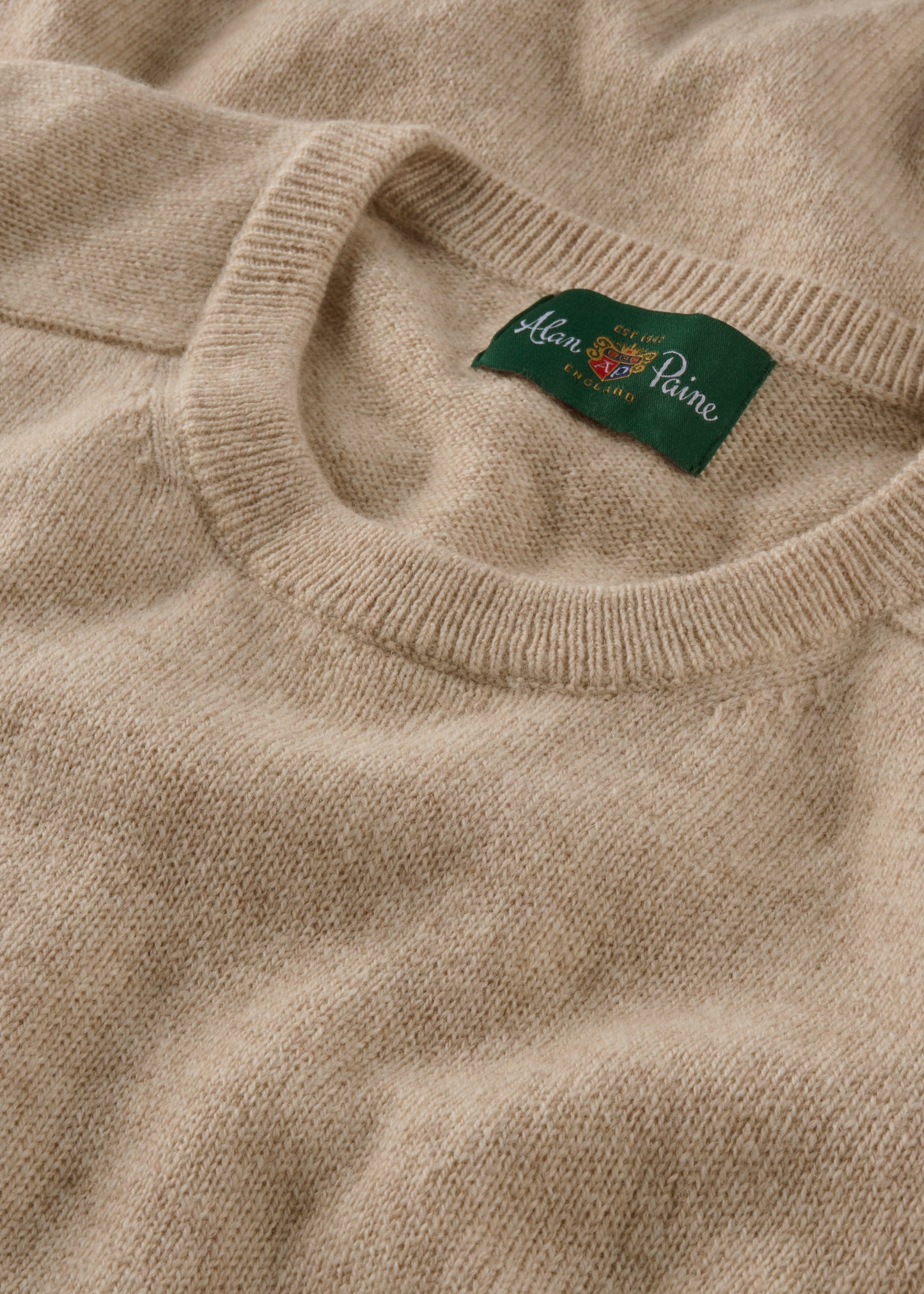 Close-up of a beige sweater with a brand label on the collar.
