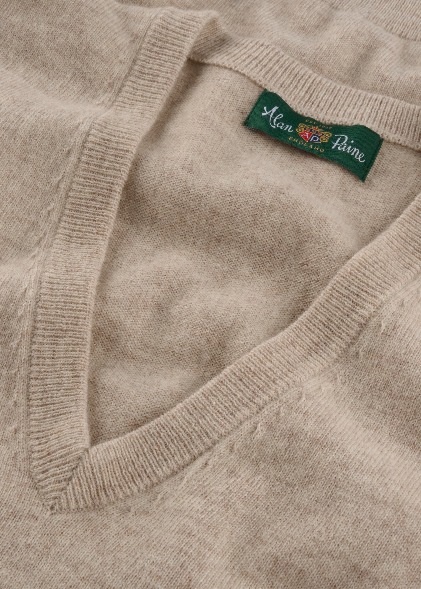 Close-up of a beige sweater with a brand label on the collar.
