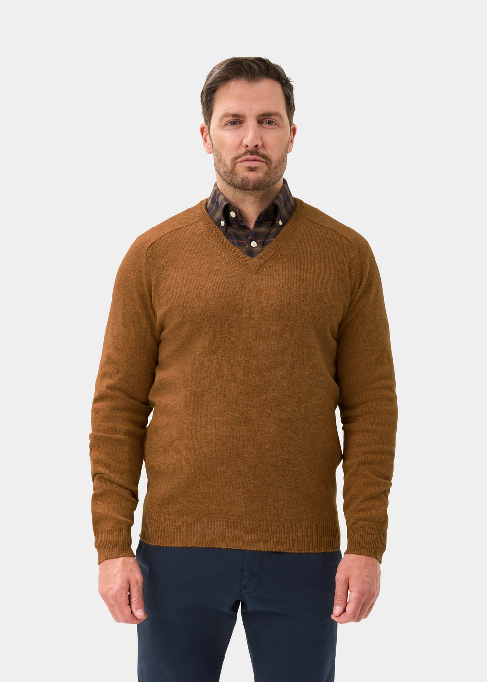 Man wears Kilsyth Lambswool V-Neck Jumper in Gazelle, regular fit, with dark pants, against a white background.