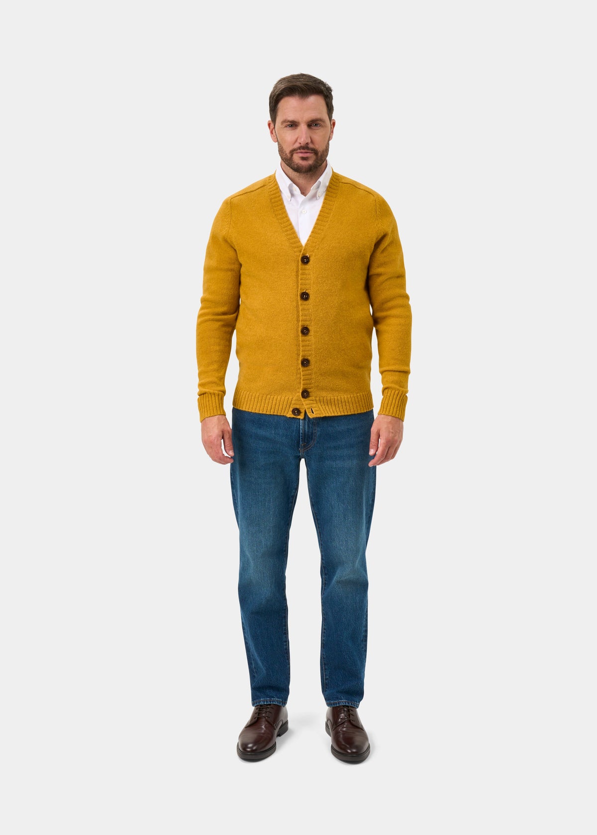 Man in Kinloch Supersoft Shetland Wool V-Neck Cardigan in Old Gold, white shirt, blue jeans, and brown shoes.