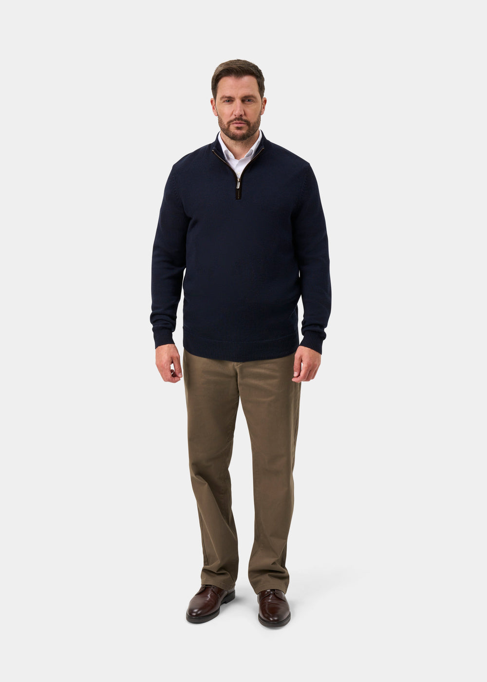 Man wears Kinmere Merino Wool Quarter Zip Jumper in dark navy, khaki pants, and brown shoes on a white background.