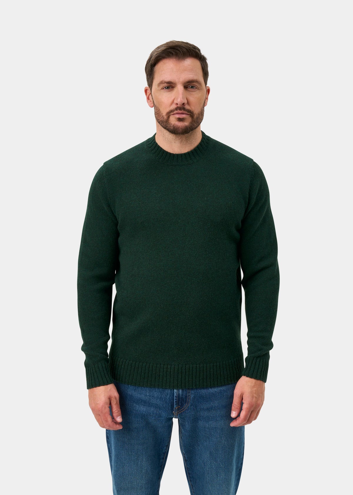 Man with short brown hair, beard, in a Kinnadie Supersoft Shetland Wool Jumper in Cossack stands by a white background.