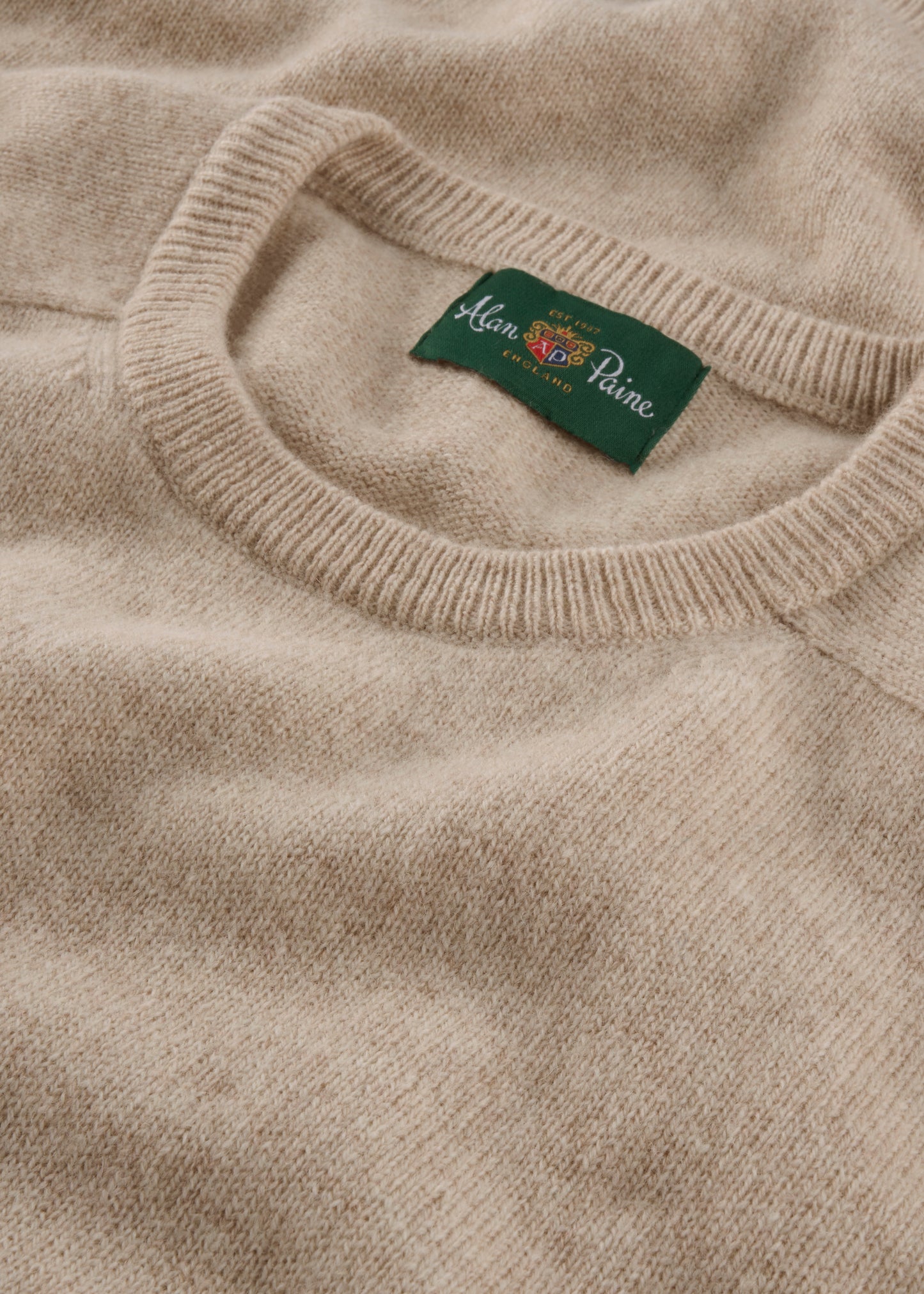 Close-up of a beige sweater with a brand label on the collar.