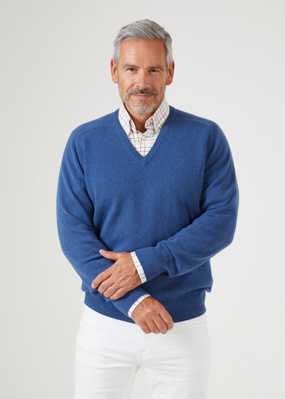 A man wears a Selkirk Pure Cashmere V-Neck Jumper In Denim over a plaid button-down shirt.
