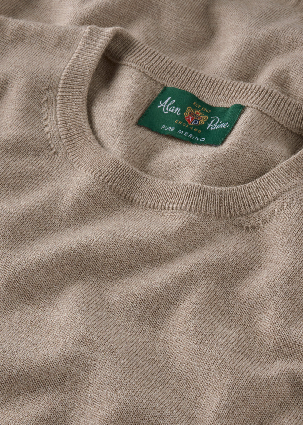 Close-up of a beige sweater with a brand label on the collar.